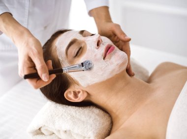 Güzel esmer kadın kozmetik maske takmaktan zevk alıyor. Rahat ve bisküvi dolu. Tıp ve kaplıca merkezi kavramlarında rahatlatıcı tedavi