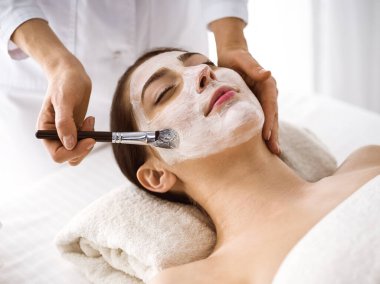 Güzel esmer kadın kozmetik maske takmaktan zevk alıyor. Rahat ve bisküvi dolu. Tıp ve kaplıca merkezi kavramlarında rahatlatıcı tedavi