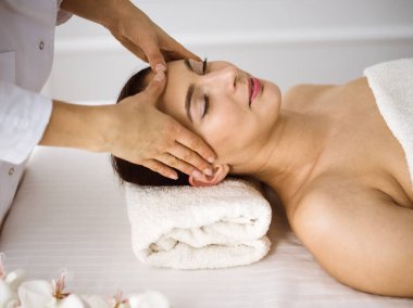 Güzel esmer kadın rahat ve bisküvi dolu yüz masajından hoşlanıyor. Tıp ve kaplıca merkezi kavramlarında rahatlatıcı tedavi