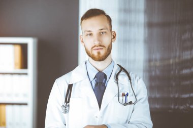 Güneşli klinikte tablet bilgisayar kullanan arkadaş canlısı kızıl sakallı doktor. Tıp konsepti