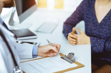 Bilinmeyen sakallı doktor ve hasta kadın güneşli klinikte otururken sağlık muayenesini tartışıyorlar.