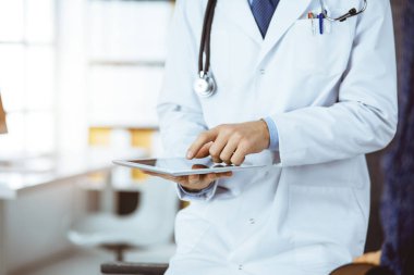 Kadın doktor ve hasta güncel sağlık muayenesini güneşli klinikte otururken tartışıyorlar.