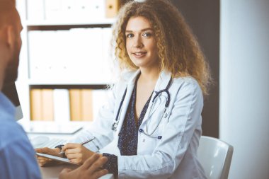 Kadın doktor ve erkek hasta güneşli klinikte otururken mevcut sağlık muayenesini tartışıyorlar.