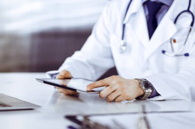 Bilinmeyen erkek doktor klinikteki tablet bilgisayarla yakın planda çalışıyor. İşteki genç doktor. Mükemmel sağlık hizmeti, tıp konsepti