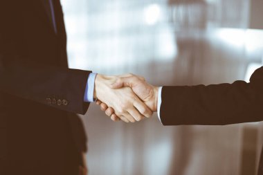 İş adamları el sıkışıyor, yakın plan. Modern bir ofiste duran bir grup tanınmamış iş adamı. Takım çalışması, ortaklık ve el sıkışma kavramı