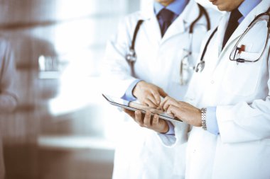 Bilinmeyen bir grup doktor hastane ofisinde dururken bazı tıbbi isim kayıtlarını kontrol etmek için bir bilgisayar tableti kullanıyor. Doktorlar hastaları muayene etmeye ve yardım etmeye hazır. Tıbbi yardım, sigorta