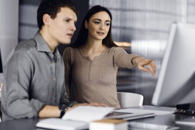 Yeşil gömlekli arkadaş canlısı genç işadamı ve programcı, modern bir ofiste masa başında bayan bir meslektaşla birlikte otururken bilgisayar üzerinde çalışıyor. Kadınlara odaklan. Başarılı olma kavramı