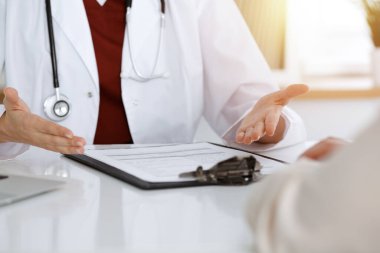 Bilinmeyen kadın doktor ve hasta güneşli klinikteki masada otururken bir şey tartışıyorlar.