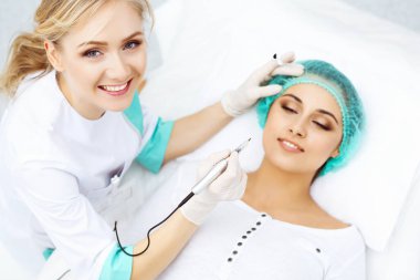 Kadın yüzüne kaş dövmesi yapan profesyonel bir güzellik uzmanı. Güzellik salonunda kalıcı kaş makyajı, yakın çekim. Kozmetoloji tedavisi