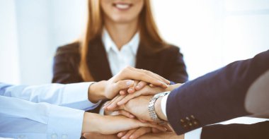 İş ekibi ellerini birleştiriyor. El ele tutuşan ve arkadaşlık, takım çalışması ve ortaklık kavramını temsil eden bir grup insan