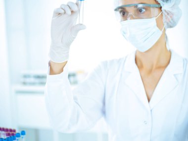 Koruyucu gözlüklü profesyonel kadın bilim adamı labaratuvarda mavi renkte reaksiyonlarla araştırma tüpü kullanıyor. Tıp ve bilim araştırmaları kavramları