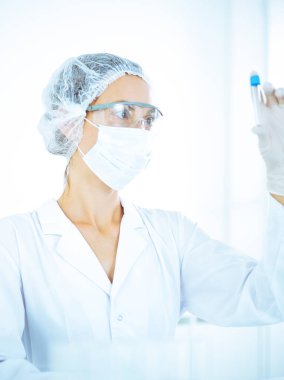 Koruyucu gözlüklü profesyonel kadın bilim adamı labaratuvarda mavi renkte reaksiyonlarla araştırma tüpü kullanıyor. Tıp ve bilim araştırmaları kavramları