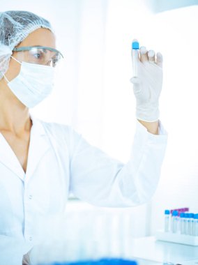 Koruyucu gözlüklü profesyonel kadın bilim adamı labaratuvarda mavi renkte reaksiyonlarla araştırma tüpü kullanıyor. Tıp ve bilim araştırmaları kavramları