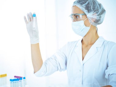 Koruyucu gözlüklü profesyonel kadın bilim adamı labaratuvarda mavi renkte reaksiyonlarla araştırma tüpü kullanıyor. Tıp ve bilim araştırmaları kavramları