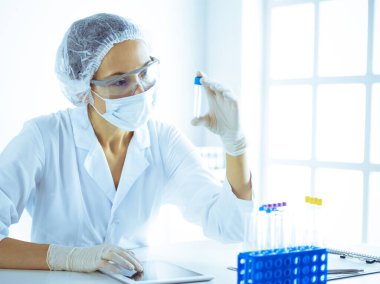 Koruyucu gözlüklü profesyonel kadın bilim adamı labaratuvarda mavi renkte reaksiyonlarla araştırma tüpü kullanıyor. Tıp ve bilim araştırmaları kavramları