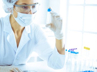 Koruyucu gözlüklü profesyonel kadın bilim adamı labaratuvarda mavi renkte reaksiyonlarla araştırma tüpü kullanıyor. Tıp ve bilim araştırmaları kavramları