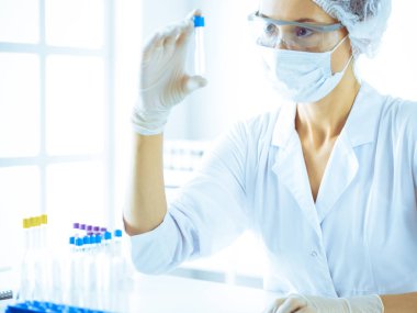 Koruyucu gözlüklü profesyonel kadın bilim adamı labaratuvarda mavi renkte reaksiyonlarla araştırma tüpü kullanıyor. Tıp ve bilim araştırmaları kavramları