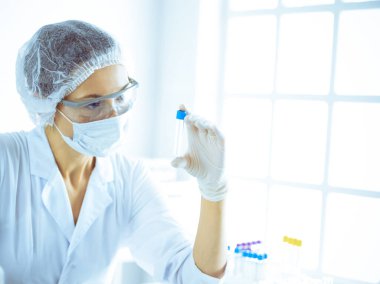 Koruyucu gözlüklü profesyonel kadın bilim adamı labaratuvarda mavi renkte reaksiyonlarla araştırma tüpü kullanıyor. Tıp ve bilim araştırmaları kavramları