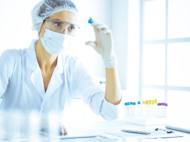 Koruyucu gözlüklü profesyonel kadın bilim adamı labaratuvarda mavi renkte reaksiyonlarla araştırma tüpü kullanıyor. Tıp ve bilim araştırmaları kavramları