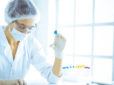 Koruyucu gözlüklü profesyonel kadın bilim adamı labaratuvarda mavi renkte reaksiyonlarla araştırma tüpü kullanıyor. Tıp ve bilim araştırmaları kavramları