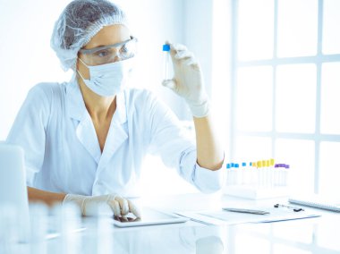 Koruyucu gözlüklü profesyonel kadın bilim adamı labaratuvarda mavi renkte reaksiyonlarla araştırma tüpü kullanıyor. Tıp ve bilim araştırmaları kavramları