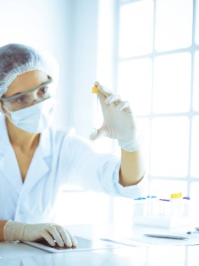 Koruyucu gözlüklü profesyonel kadın bilim adamı labaratuvarda mavi renkte reaksiyonlarla araştırma tüpü kullanıyor. Tıp ve bilim araştırmaları kavramları