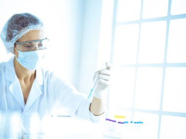 Koruyucu gözlüklü profesyonel kadın bilim adamı labaratuvarda mavi renkte reaksiyonlarla araştırma tüpü kullanıyor. Tıp ve bilim araştırmaları kavramları