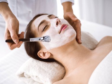 Güzel esmer kadın kozmetik maske takmaktan zevk alıyor. Rahat ve bisküvi dolu. Tıp ve kaplıca merkezi kavramlarında rahatlatıcı tedavi