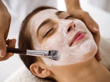 Güzel esmer kadın kozmetik maske takmaktan zevk alıyor. Rahat ve bisküvi dolu. Tıp ve kaplıca merkezi kavramlarında rahatlatıcı tedavi