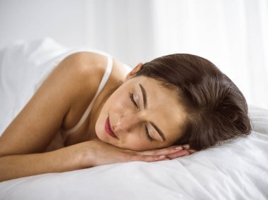 Güzel, genç, esmer kadın yatakta rahat ve mutlu bir şekilde yatarken uyuyor. Günaydın konsept.