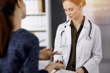 Neşeli gülümseyen kadın doktor ve hasta kadın güncel sağlık muayenesini güneşli klinikte otururken tartışıyorlar. Hastanede mükemmel bir tıbbi hizmet. Tıp konsepti