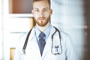 Kızıl sakallı doktor çalışma yerinin yanındaki güneşli klinikte dikiliyor. Tıp konsepti