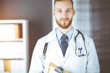 Dost canlısı kızıl sakallı doktor güneşli klinikte panoya yazı yazıyor. Tıp konsepti