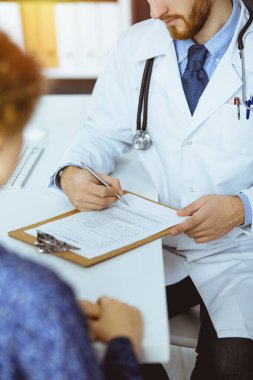 Bilinmeyen sakallı doktor ve hasta kadın güneşli klinikte otururken sağlık muayenesini tartışıyorlar.