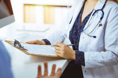 Kadın doktor ve hasta güncel sağlık muayenesini güneşli klinikte otururken tartışıyorlar.