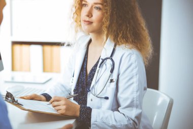 Kadın doktor ve erkek hasta güneşli klinikte otururken mevcut sağlık muayenesini tartışıyorlar.