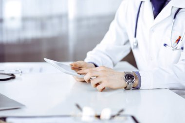 Bilinmeyen erkek doktor klinikteki tablet bilgisayarla yakın planda çalışıyor. İşteki genç doktor. Mükemmel sağlık hizmeti, tıp konsepti