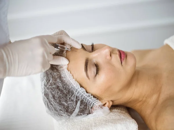 Beautician doing beauty procedure with syringe to face of young brunette woman in sunny clinic. Cosmetic medicine and surgery, beauty injections