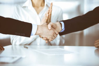 İş adamları toplantıda ya da pazarlıkta el sıkışıyor, yakın plan. Bilinmeyen iş adamları grubu ve modern bir ofiste arka planda bir kadın. Takım çalışması, ortaklık ve el sıkışma kavramı