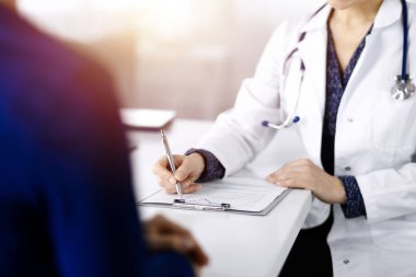 Bilinmeyen kadın-doktor, bir klinikteki güneşli dolapta birlikte otururken hastasına bazı tıbbi tavsiyeler yazıyor. Doktor bir pano kullanıyor, yakın plan.