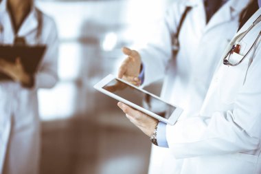 Bir grup doktor, elinde not panosu olan bir hemşire hastane ofisinde yan yana dururken bazı notlar alırken bilgisayar tabletinde tıbbi isimleri kontrol ediyorlar. Doktorlar incelemeye hazır ve...