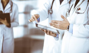 Bilinmeyen bir grup doktor hastane ofisinde dururken bazı tıbbi isim kayıtlarını kontrol etmek için bir bilgisayar tableti kullanıyor. Doktorlar hastaları muayene etmeye ve yardım etmeye hazır. Tıbbi yardım, sigorta