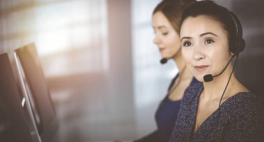 İki iş kadını, güneşli bir modern ofiste masada otururken, müşterilerle kulaklıkla sohbet ediyorlar. Çağrı merkezinde çeşitli insanlar. Tele pazarlama ve müşteri hizmetleri