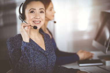 İki iş kadını, güneşli bir modern ofiste masada otururken, müşterilerle kulaklıkla sohbet ediyorlar. Çağrı merkezinde çeşitli insanlar. Tele pazarlama ve müşteri hizmetleri