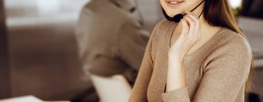 Modern bir ofiste meslektaşıyla birlikte masa başında otururken, kulaklıklı genç bir kız bir firma müşterisiyle konuşuyor. İş yerindeki çağrı merkezi operatörleri