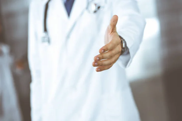 Unknown man-doctor standing straight and offering helping hand in modern clinic. Female colleague is in a hurry at the background of physician. Medicine concept