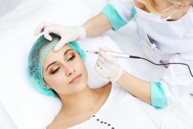 Kadın yüzüne kaş dövmesi yapan profesyonel bir güzellik uzmanı. Güzellik salonunda kalıcı kaş makyajı, yakın çekim. Kozmetoloji tedavisi