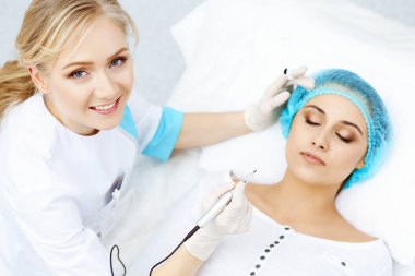 Kadın yüzüne kaş dövmesi yapan profesyonel bir güzellik uzmanı. Güzellik salonunda kalıcı kaş makyajı, yakın çekim. Kozmetoloji tedavisi