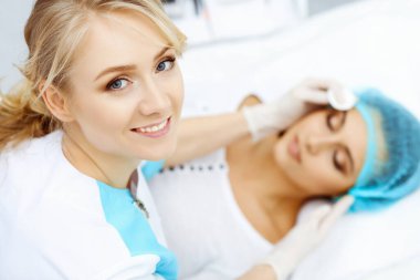 Güzellik salonunda profesyonel güzellik uzmanı ve genç bir kadın. Makyöz, müşteri tenine pamuk pedlerle dokunuyor, yakın plan. Kozmetik, yüz, güzellik ve kaplıca