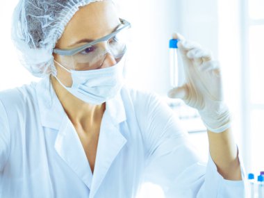 Koruyucu gözlüklü profesyonel kadın bilim adamı labaratuvarda mavi renkte reaksiyonlarla araştırma tüpü kullanıyor. Tıp ve bilim araştırmaları kavramları